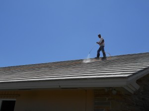 Man using power washer on roof of home.